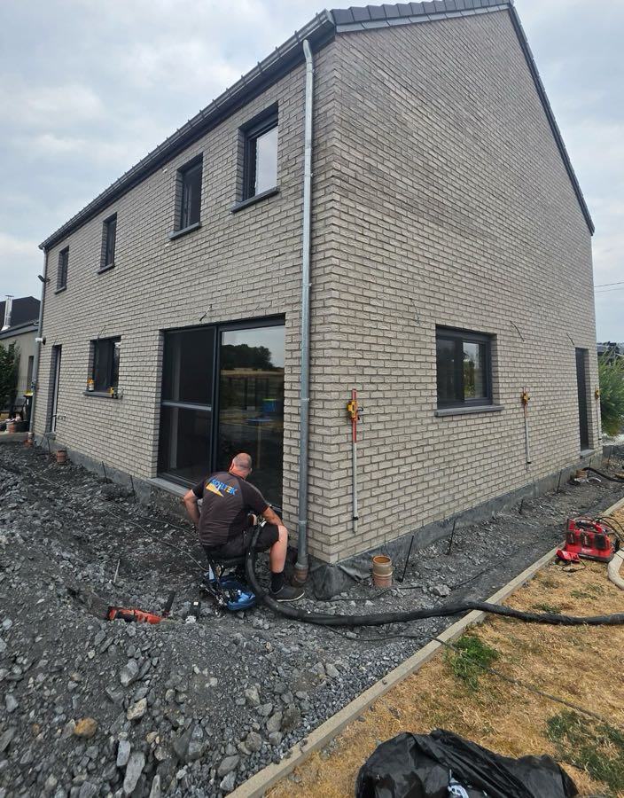 Soiltek-medewerker injecteert expansiehars langs de gevel van een woning, met laserontvangers op de muur