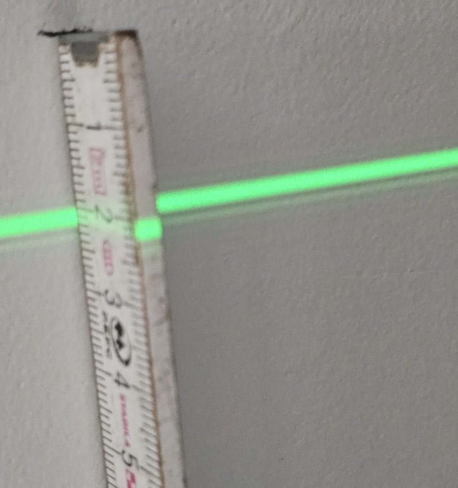 Groene laserlijn op een meetlat tegen een binnenmuur