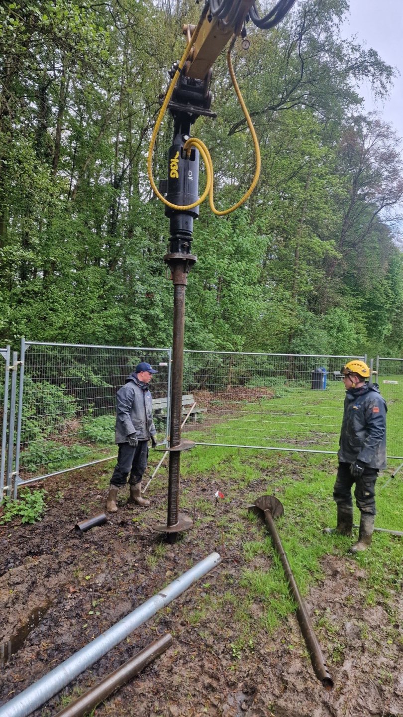 Plaatsing van een schroefpaal met een graafkraan tussen de bomen in Nieuwenhoven