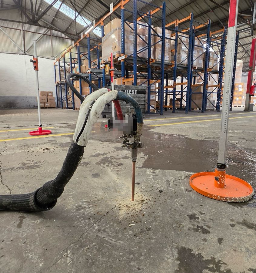 Injectie van expansiehars door een betonvloer in een magazijn, met laserontvangers op statief