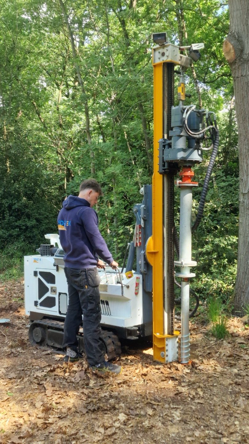 Compacte rupsmachine plaatst een schroefpaal tussen de bomen